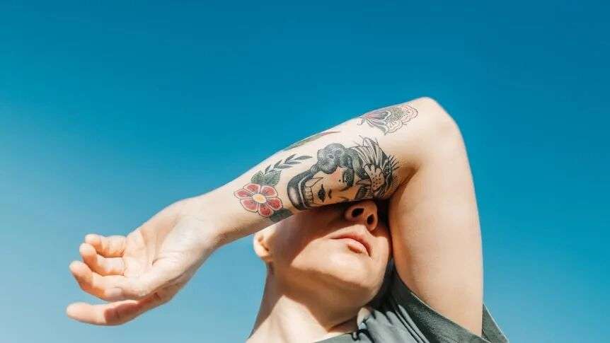A person covers their eyes with their tattooed arm.