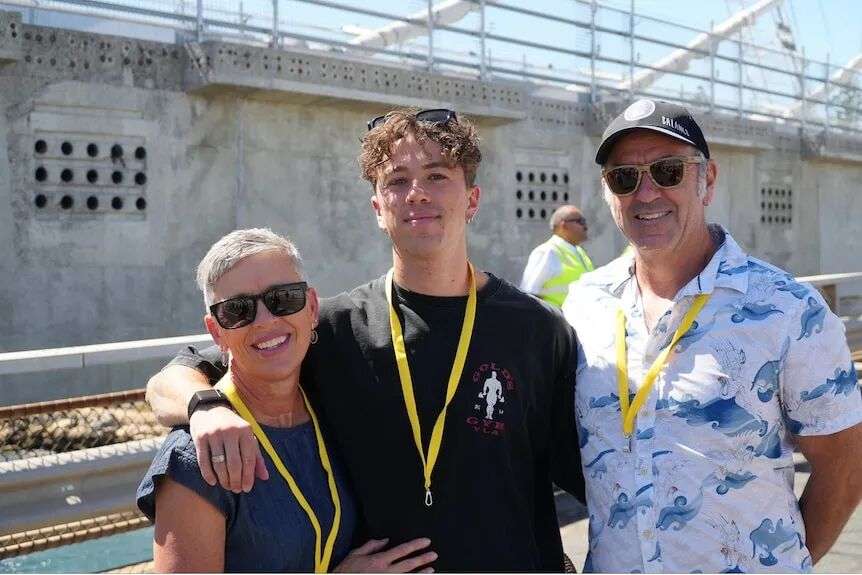A young man in a black t-shirt with his mother to his left and father to his right