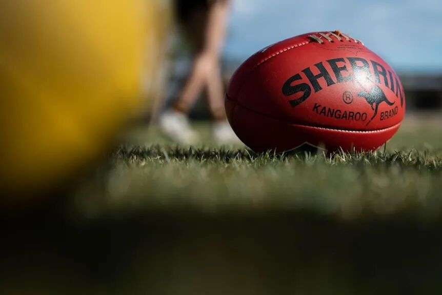 A red Sherrin Aussie Rules football on grass.