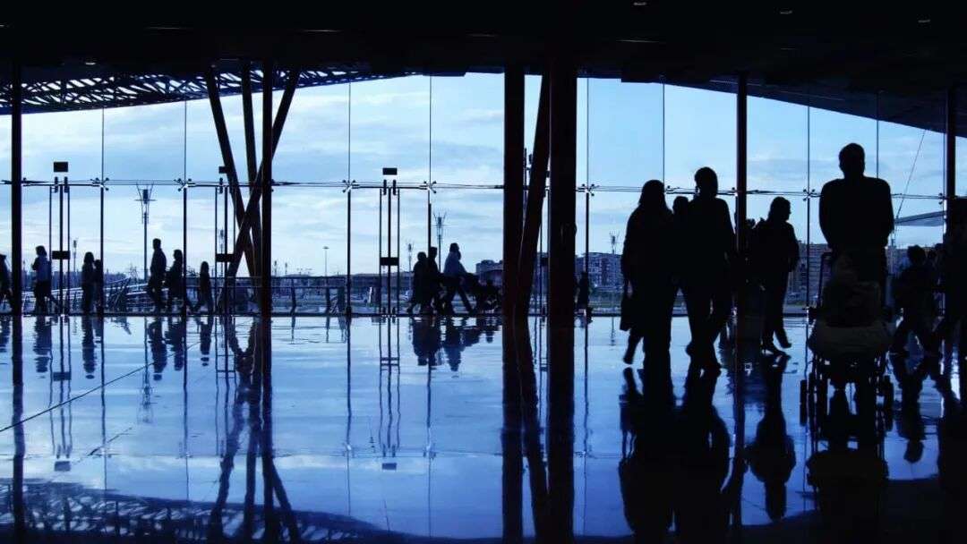 Several travellers are seen milling about in an dimly lit airport terminal.