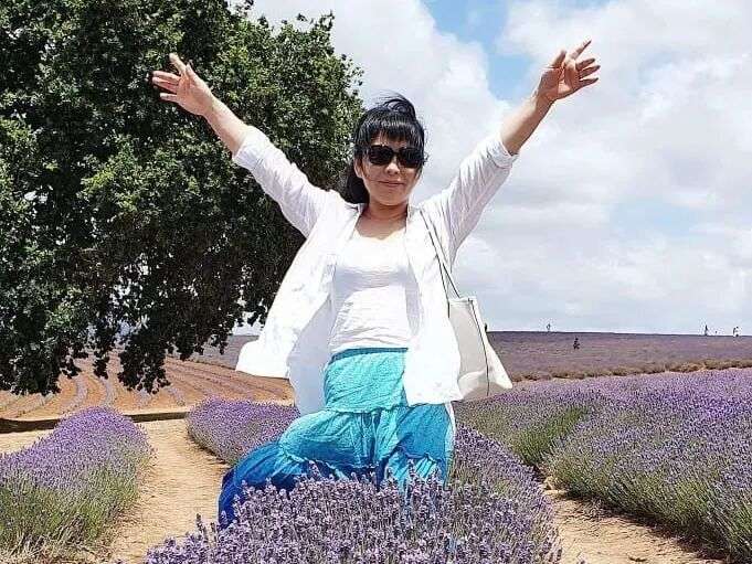 A woman stands above lavender bushes with her arms in the air.