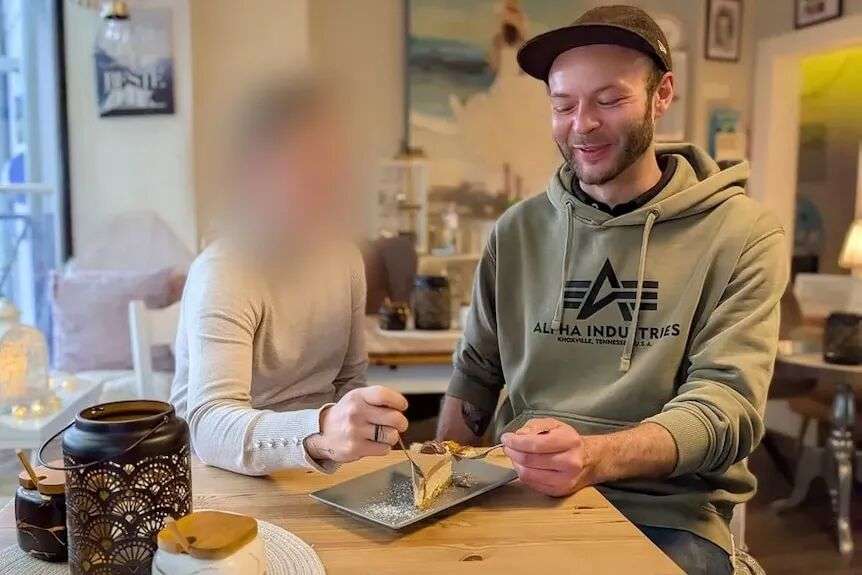 A young man and a woman sit at a table in a cafe eating a slice of cake.
