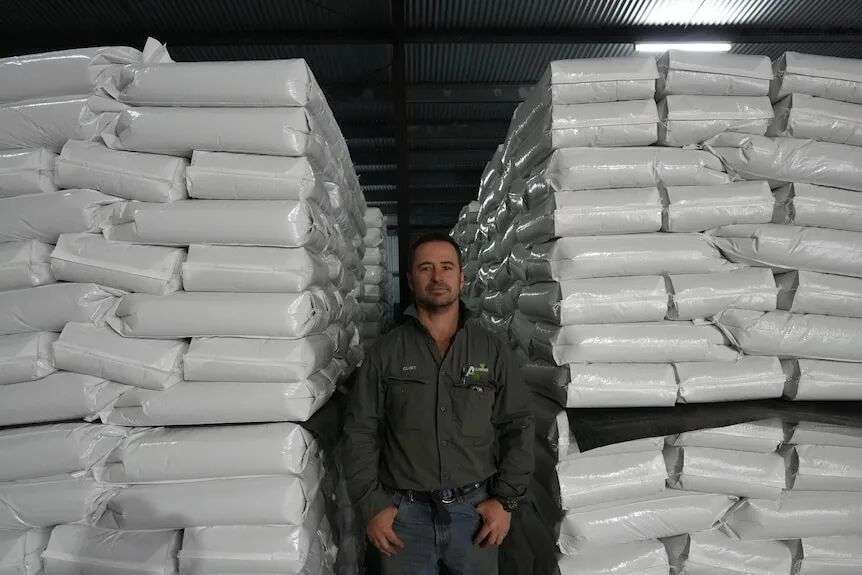 Clint Allenden stands in a dark shed between two stacks of white mungbean sacks with his hands in his pockets.