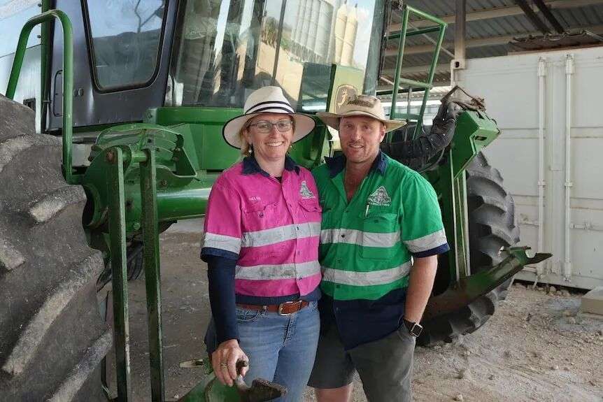 Stuart and Helen Johnston stand in front of their large green tractor-like machine with their arms around each other.