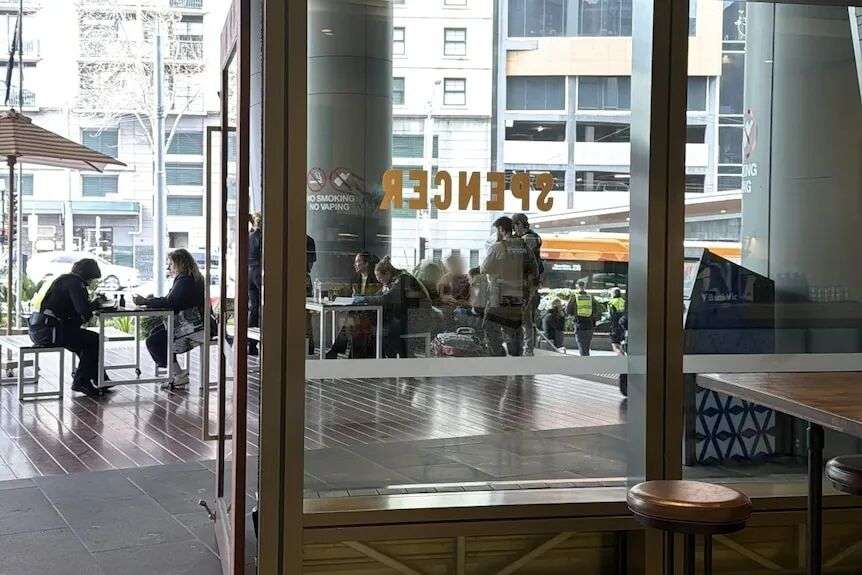 A photo taken from inside a cafe looking through the glass doors to police standing near a boy and woman.